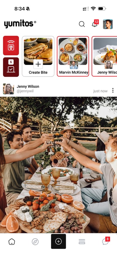 A Yumitos feed with a friend's post: a long outdoor table where friends raise a toast over a spread of fruit, cheese and bread